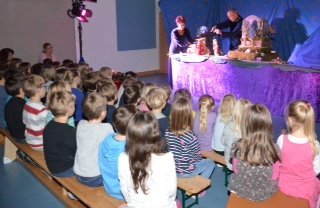 Kinder sitzen auf Bänken und schauen das Figurentheater an