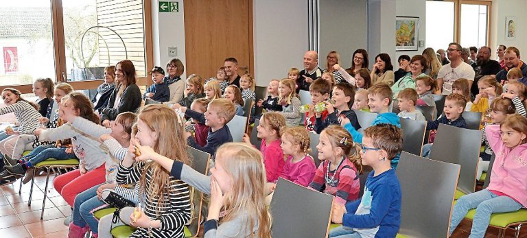 Kinder sitzen in den vorderen Stuhlreihen und lachen, im hinteren Bereich sitzen die Eltern